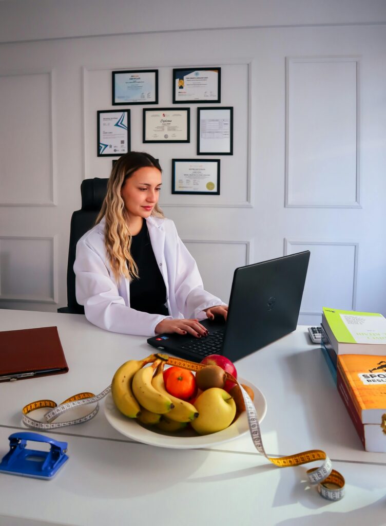 Home Dietitian at desk with fruits and laptop, representing healthy lifestyle and nutrition consultancy.