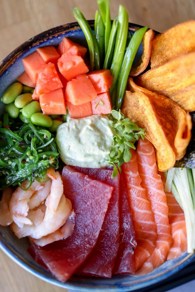 Home Delicious poke bowl with fresh seafood, vegetables, and creamy sauce.