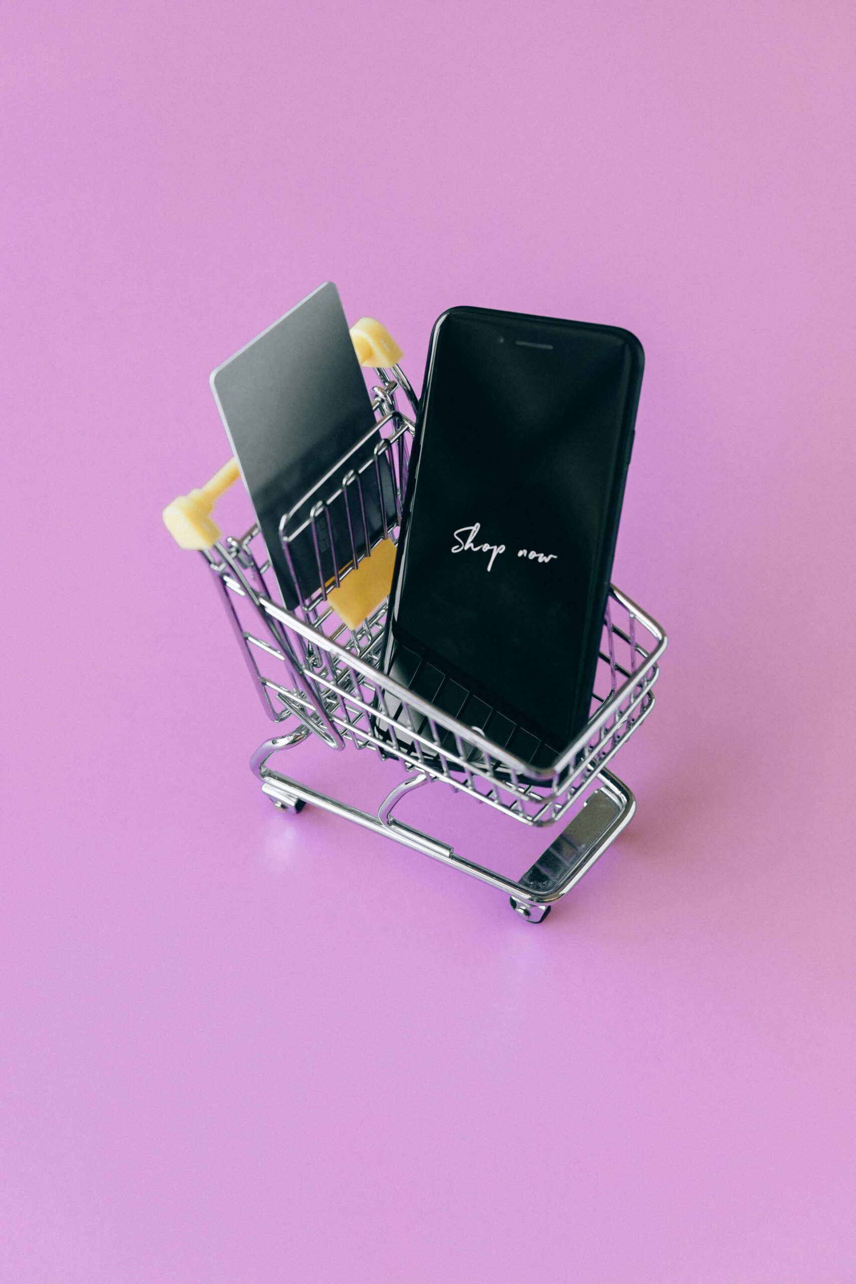 Home Modern shopping concept featuring smartphone and credit cards in a miniature cart on pink background.